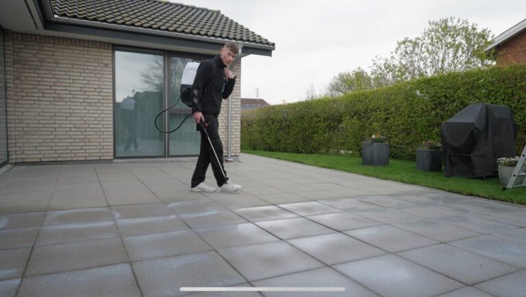 Mand rengør terrassefliser med rygsprøjte